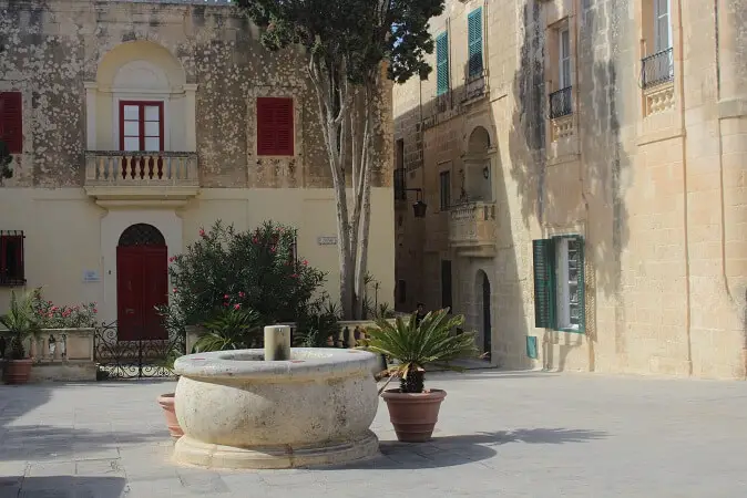 Square in Mdina surrounded by honey colored buildings with red and blue doors
